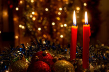 Three red candles with Christmas balls and dark background with lights.