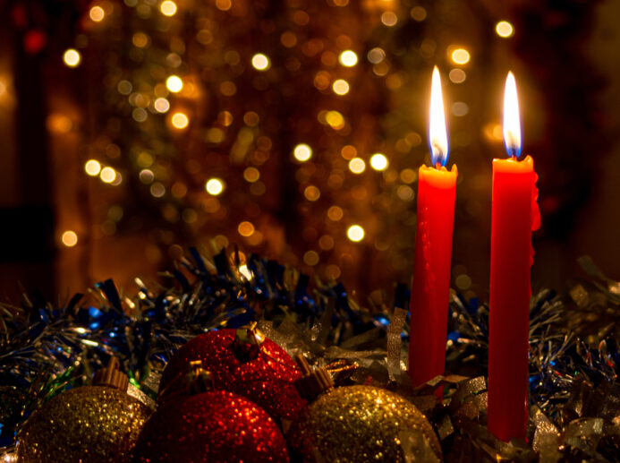 Three red candles with Christmas balls and dark background with lights.