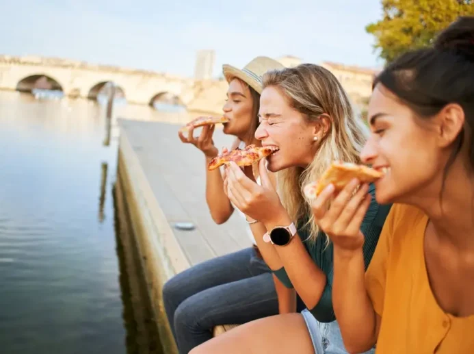 Tři mladé ženy jedí pizzu a usmívají se.