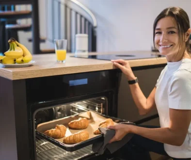 Mladá žena se usmívá a drží v ruce plech s croissanty.