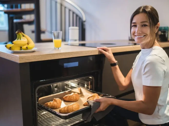 Mladá žena se usmívá a drží v ruce plech s croissanty.