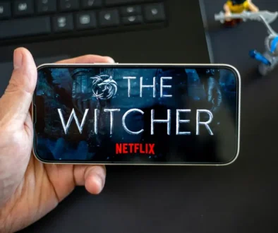 Ruka s telefonem, kde je logo Netflixu a The Witcher. Pod ním jsou postavičky.