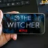 Ruka s telefonem, kde je logo Netflixu a The Witcher. Pod ním jsou postavičky.