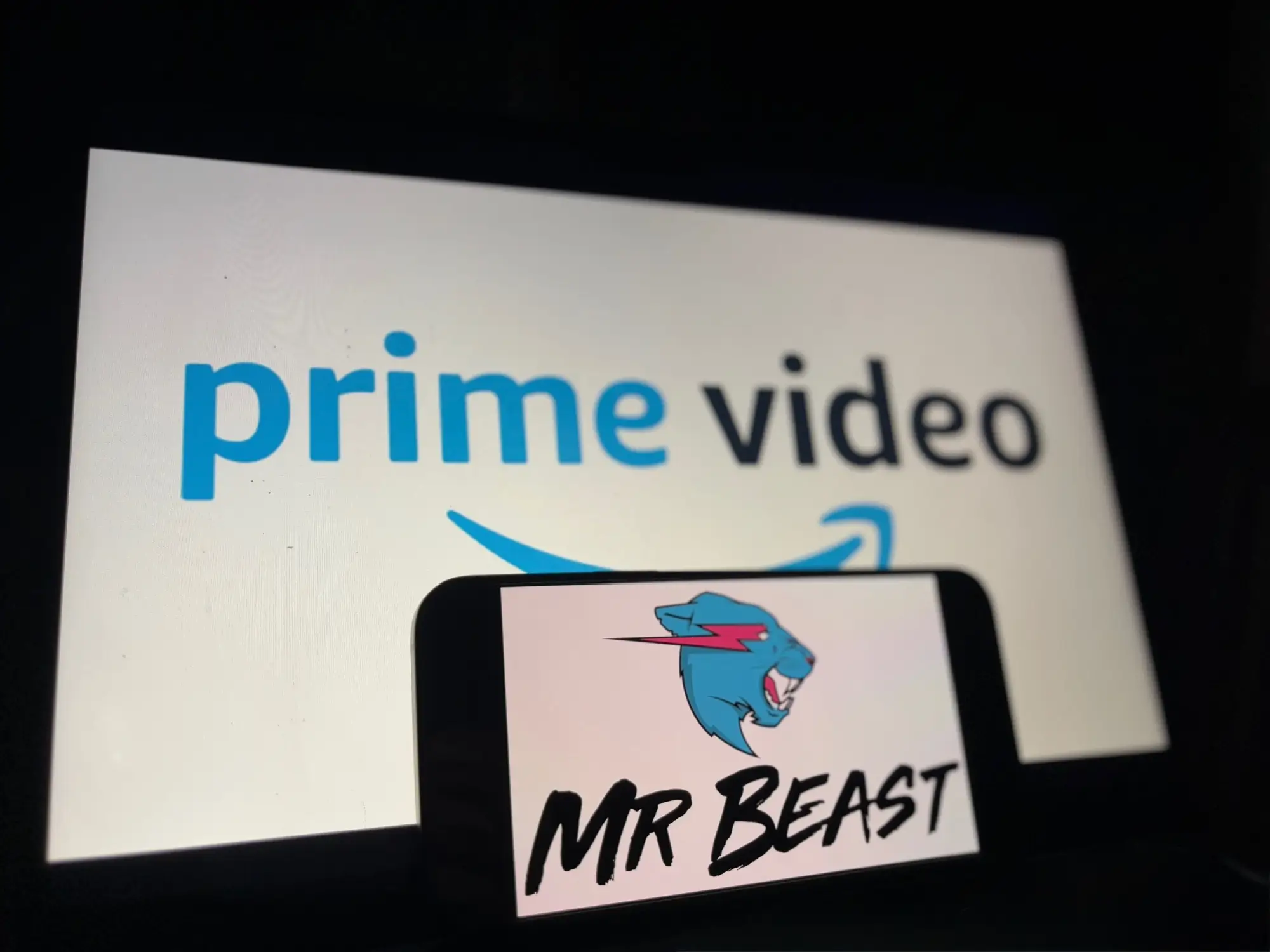 mobil zobrazující logo Mr Beast nacházející se pod obrazovkou zobrazující logo Prime Video