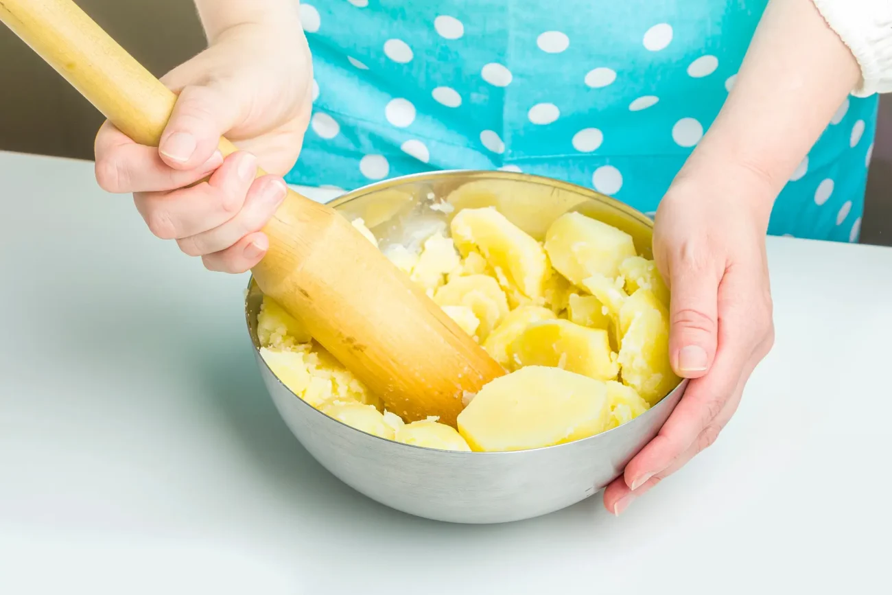 Žena drží misku plnou brambor a šťouchá je. 